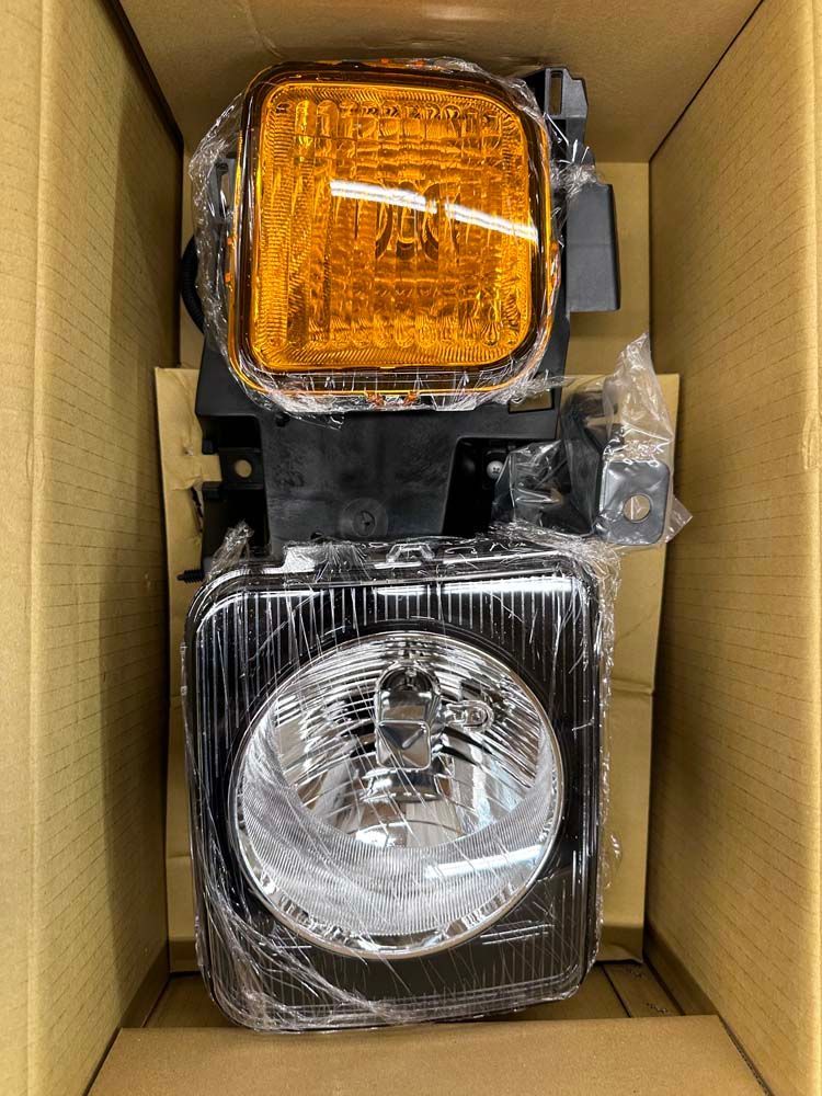 A pair of headlights are wrapped in plastic and sitting in a cardboard box.