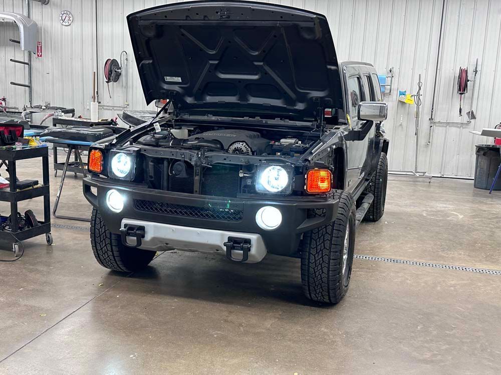 A black hummer with the hood up is parked in a garage.