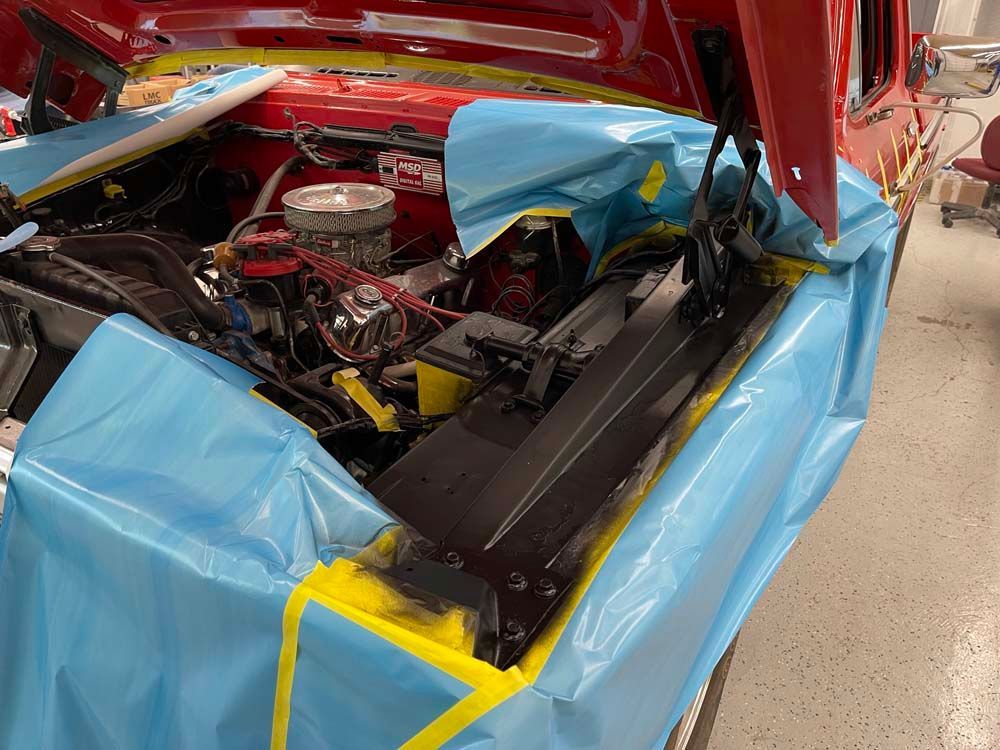 The hood of a red car is wrapped in blue plastic and yellow tape.