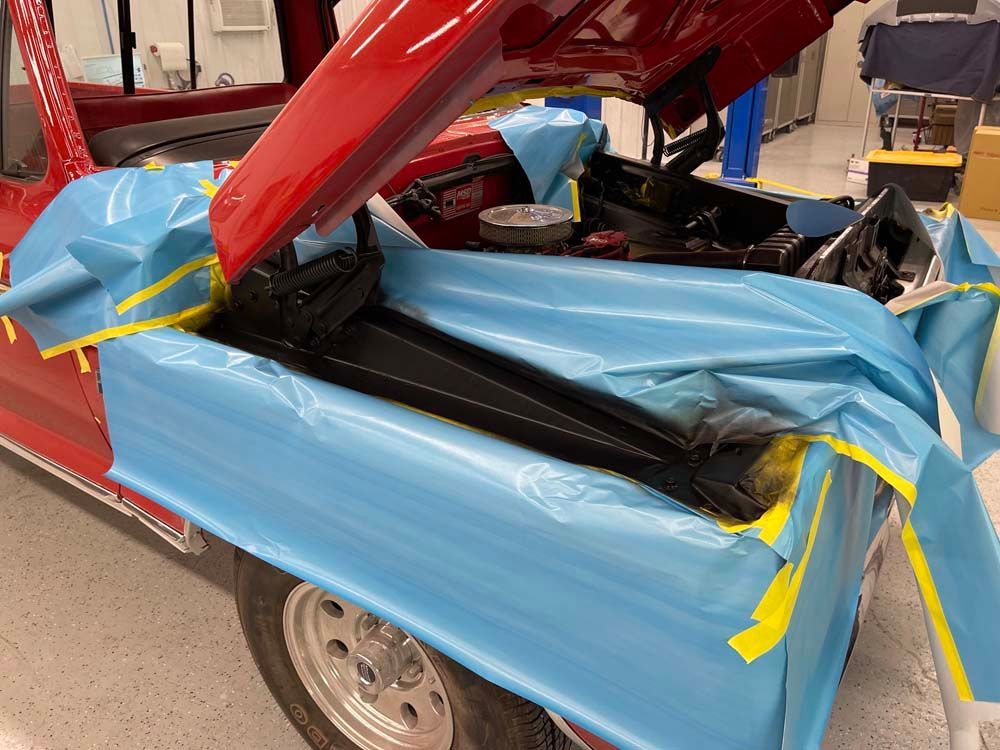 A red car with the hood open is wrapped in blue plastic
