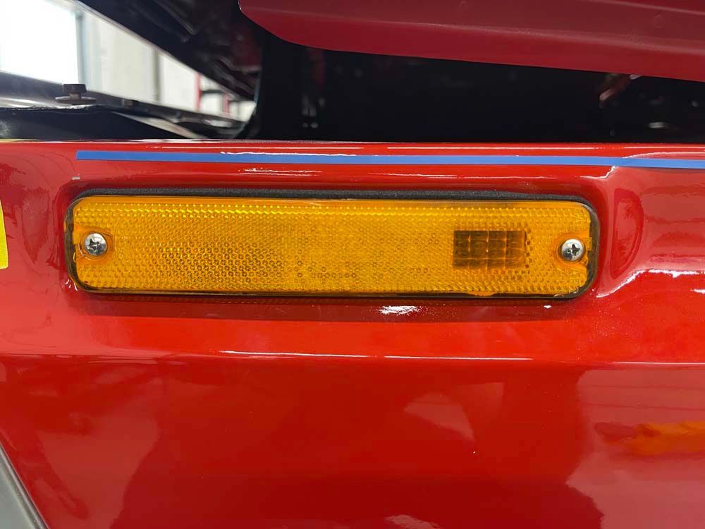 A close up of a yellow reflector on the side of a red car.