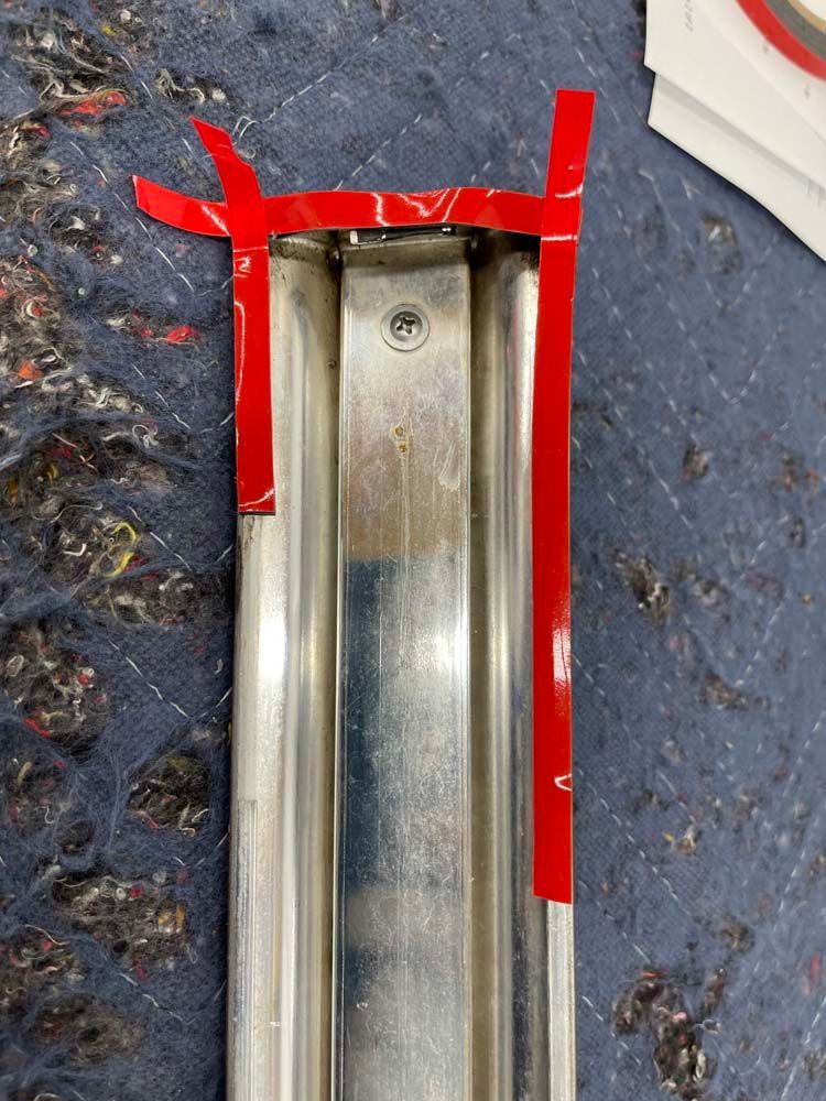 A piece of metal with red tape on it is sitting on a blue surface.