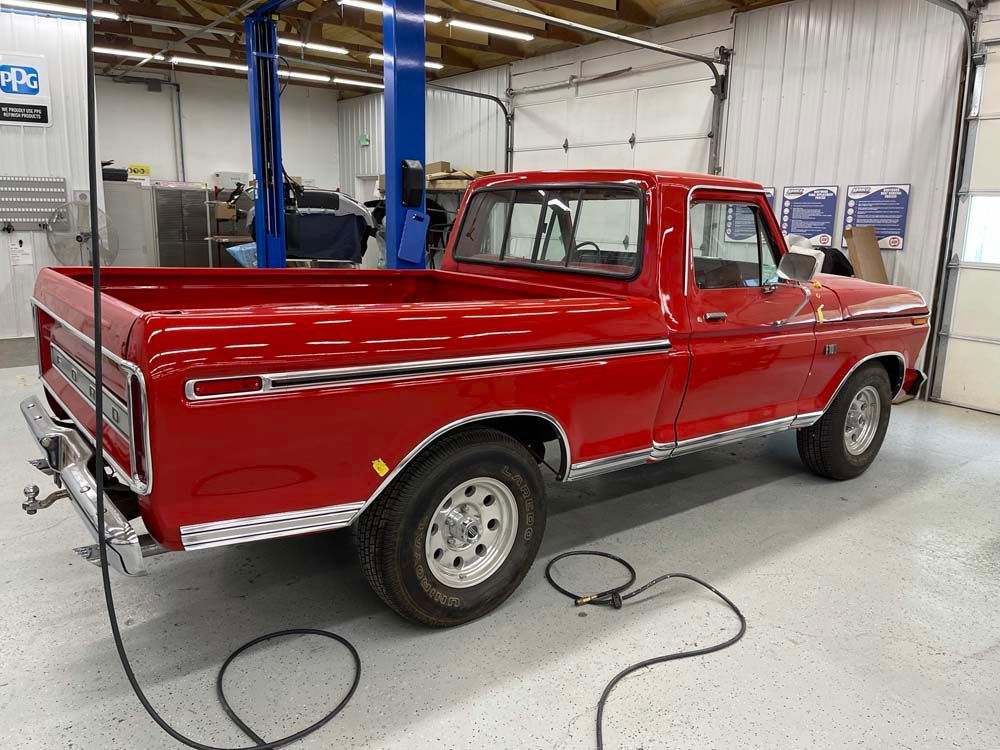 A red truck is parked in a garage next to a lift.