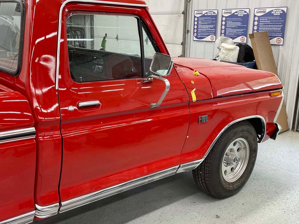 A red truck is parked in a garage with signs on the wall behind it