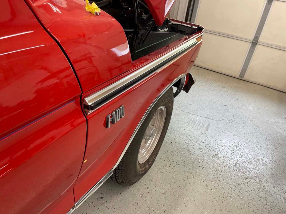 A red ford truck is parked in a garage with the hood open.