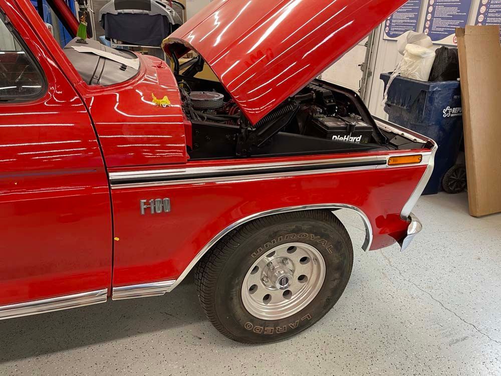 A red ford truck with the hood up in a garage