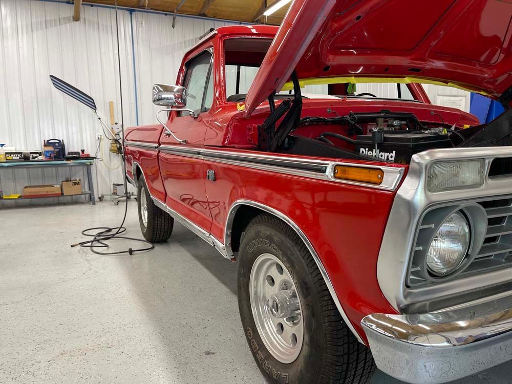 A red truck with the hood up is parked in a garage.