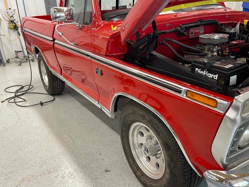 A red truck with the hood up is parked in a garage.