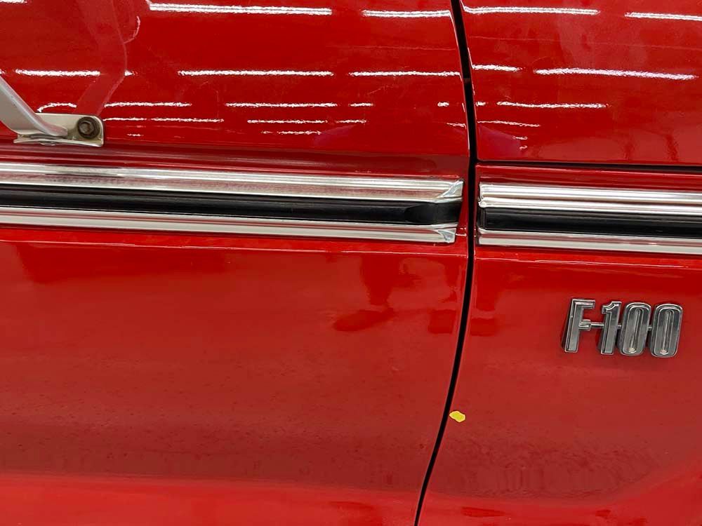 A red ford f100 truck is parked in a garage.