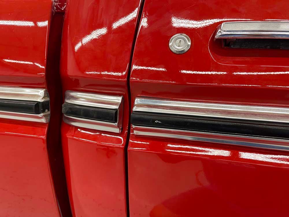 A close up of a red car door with a chrome trim.