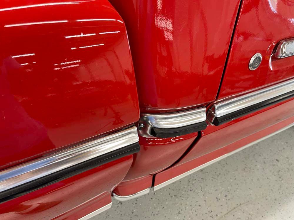 A red car with chrome trim is parked in a garage.