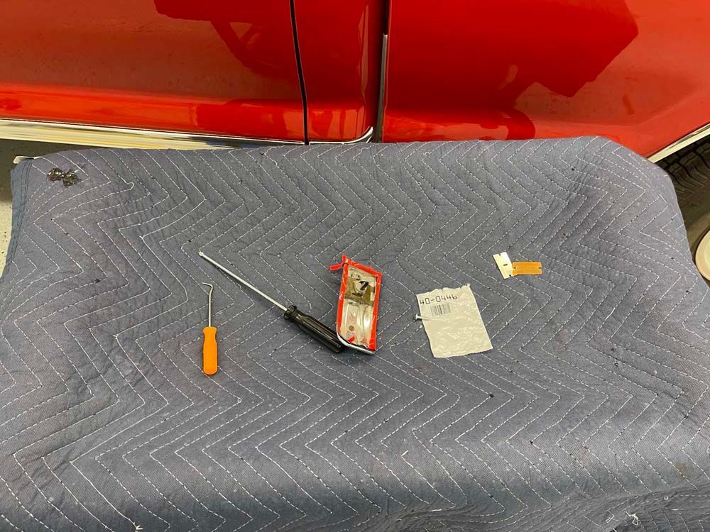 A red truck is parked behind a blue blanket with tools on it.