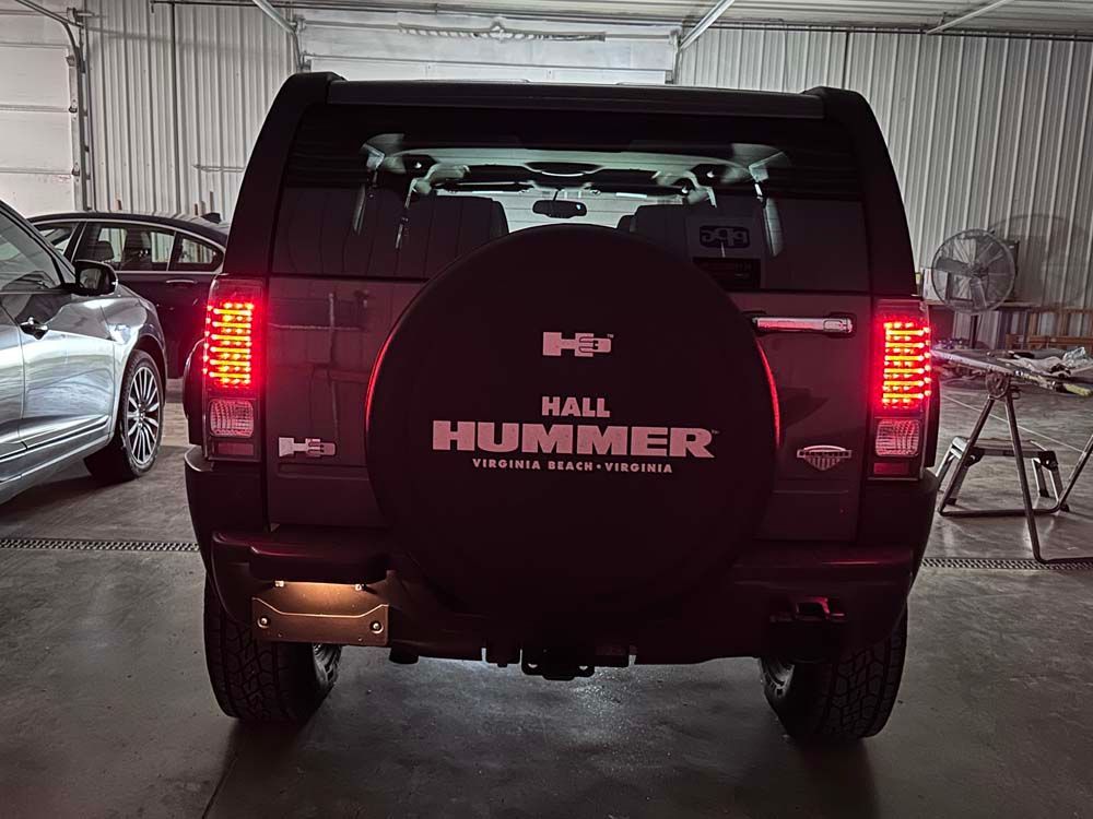 A black hummer is parked in a garage with other cars.