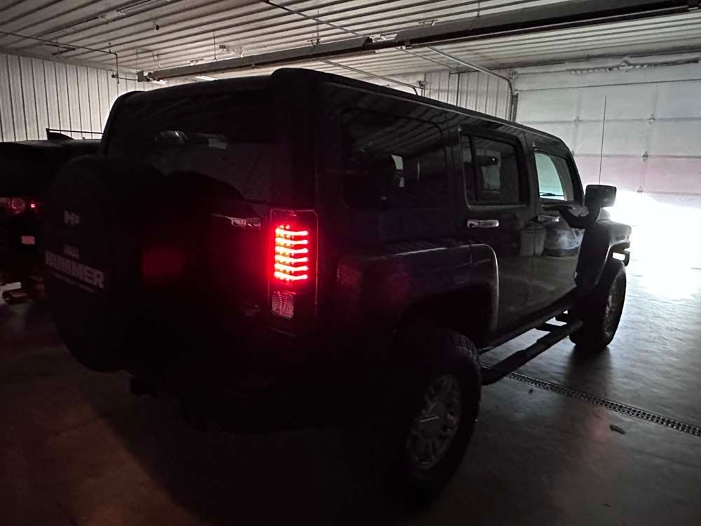 A black hummer is parked in a garage with its lights on.