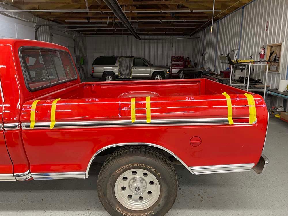 A red truck with yellow tape on the bed is parked in a garage.