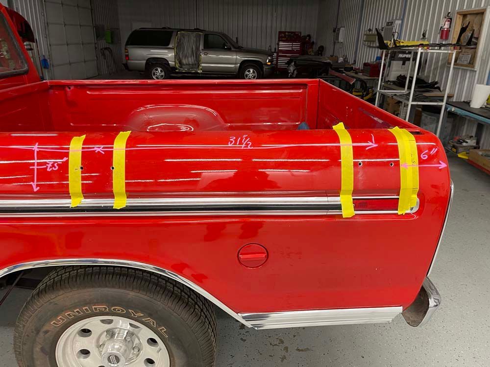 A red truck is sitting in a garage with yellow tape on the bed.