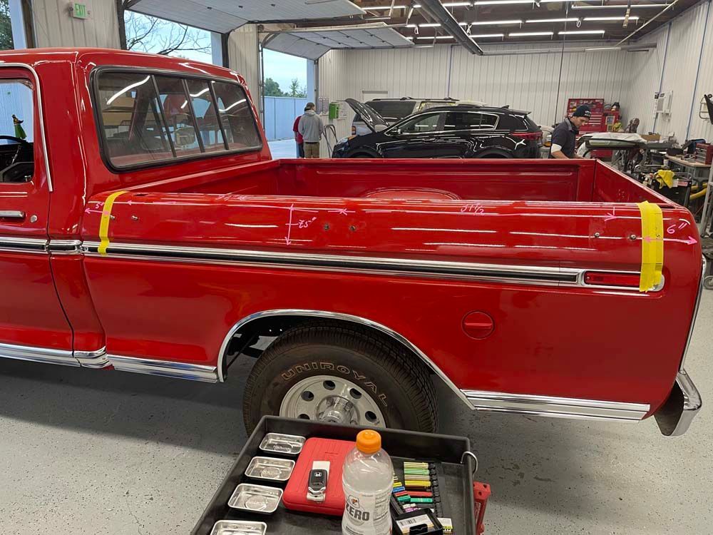 A red truck is parked in a garage with a yellow tape on the bed.