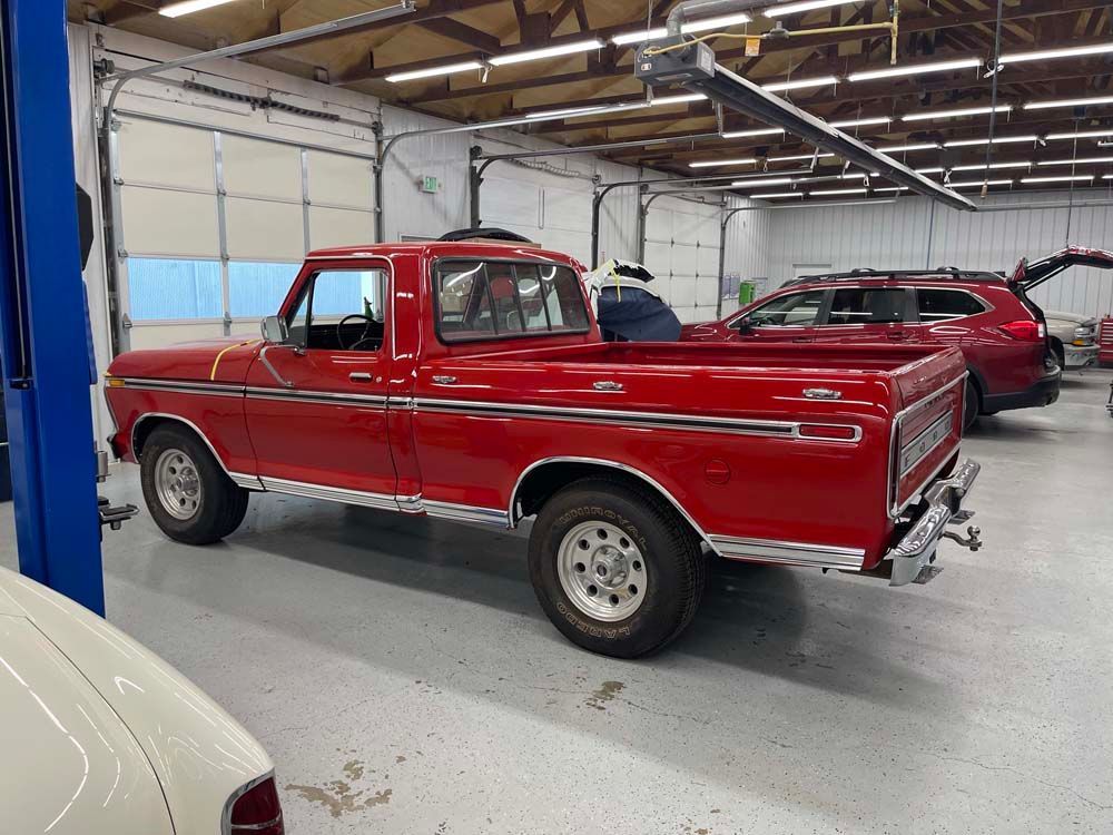 A red truck is parked in a garage next to a white car.