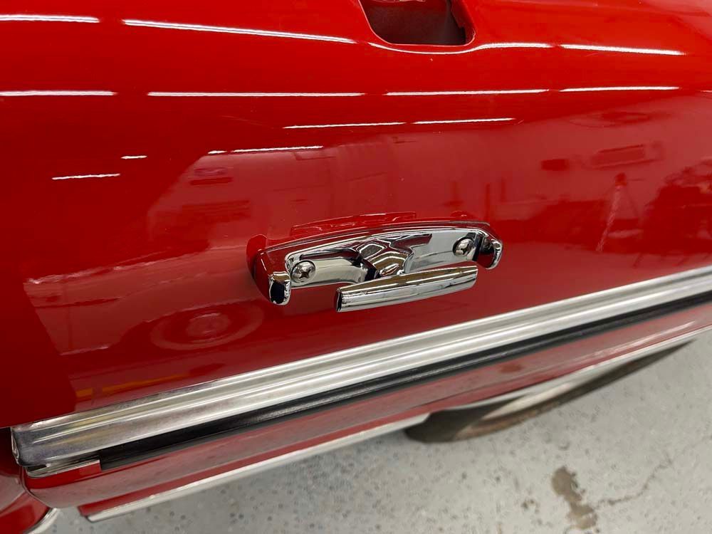 A red car is parked in a garage with a chrome handle on the door.