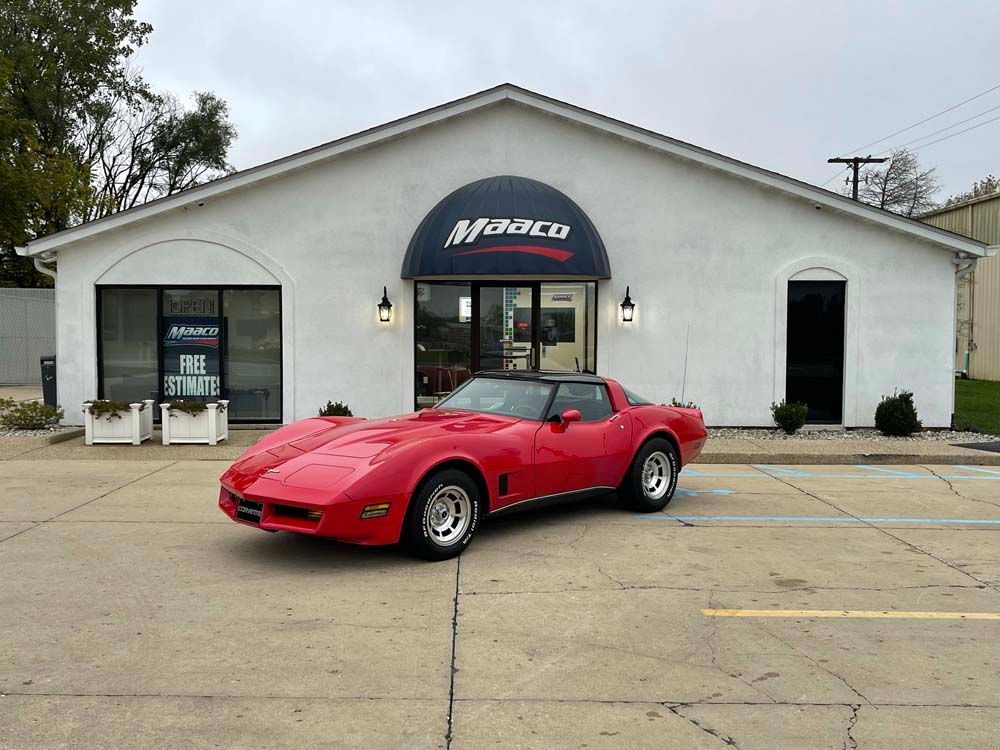 A red corvette is parked in front of a white building.