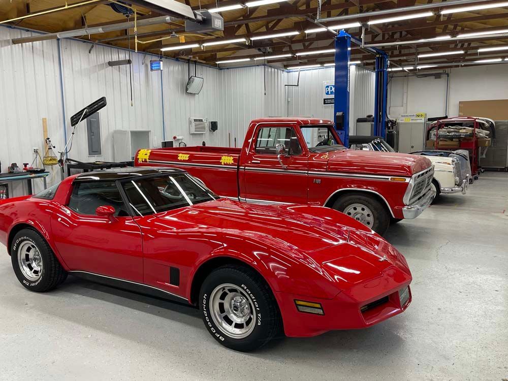 A red corvette and a red truck are parked in a garage.