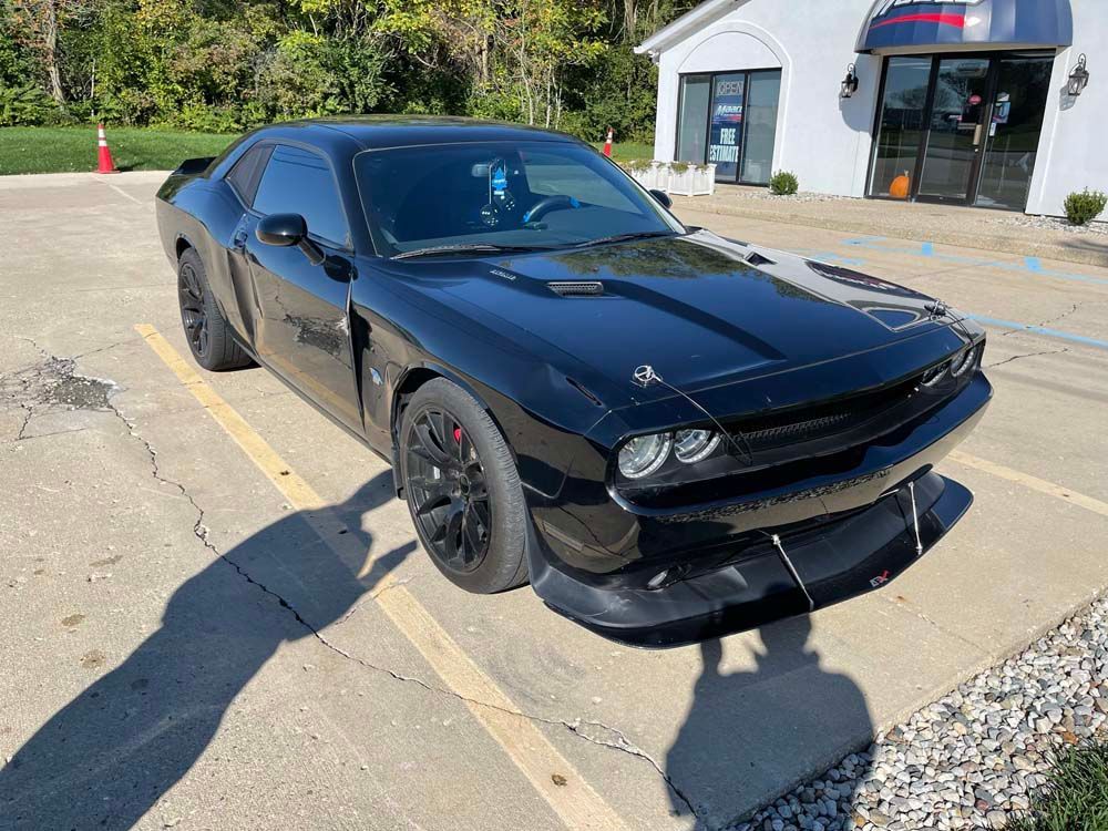 A black dodge challenger is parked in a parking lot in front of a building.