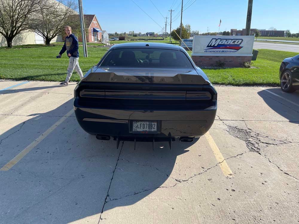 A black car is parked in a parking lot in front of a marco sign.
