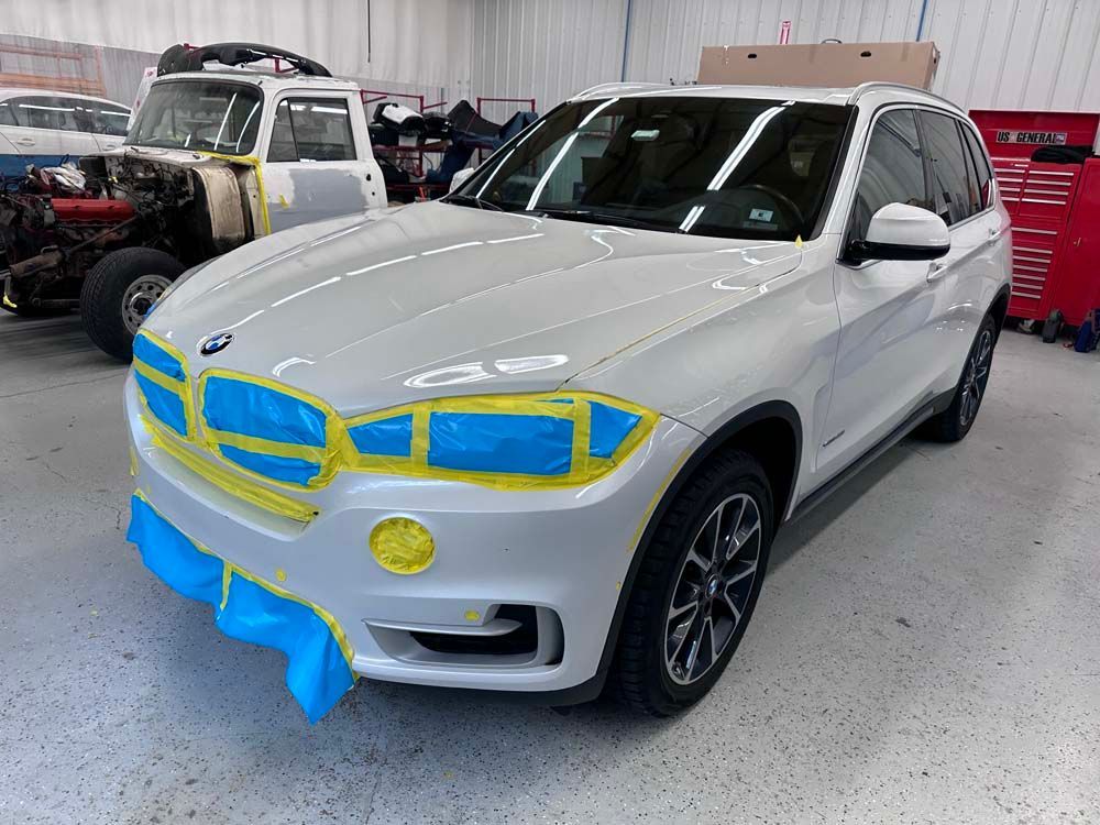 A white bmw x5 is being painted in a garage.