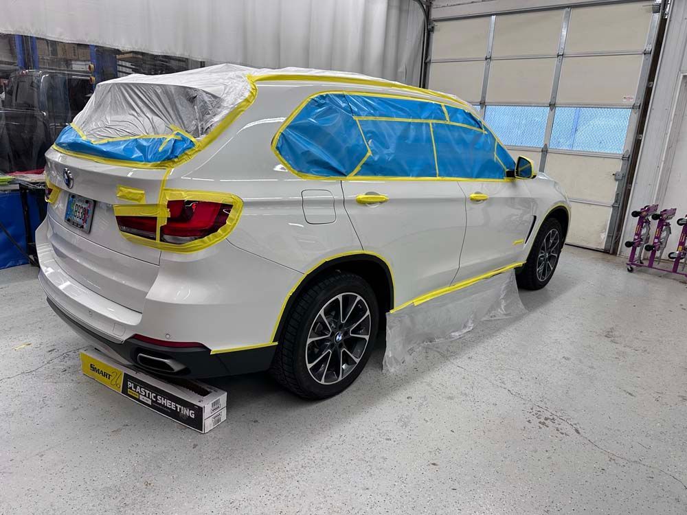 A white bmw x5 is being painted in a garage.