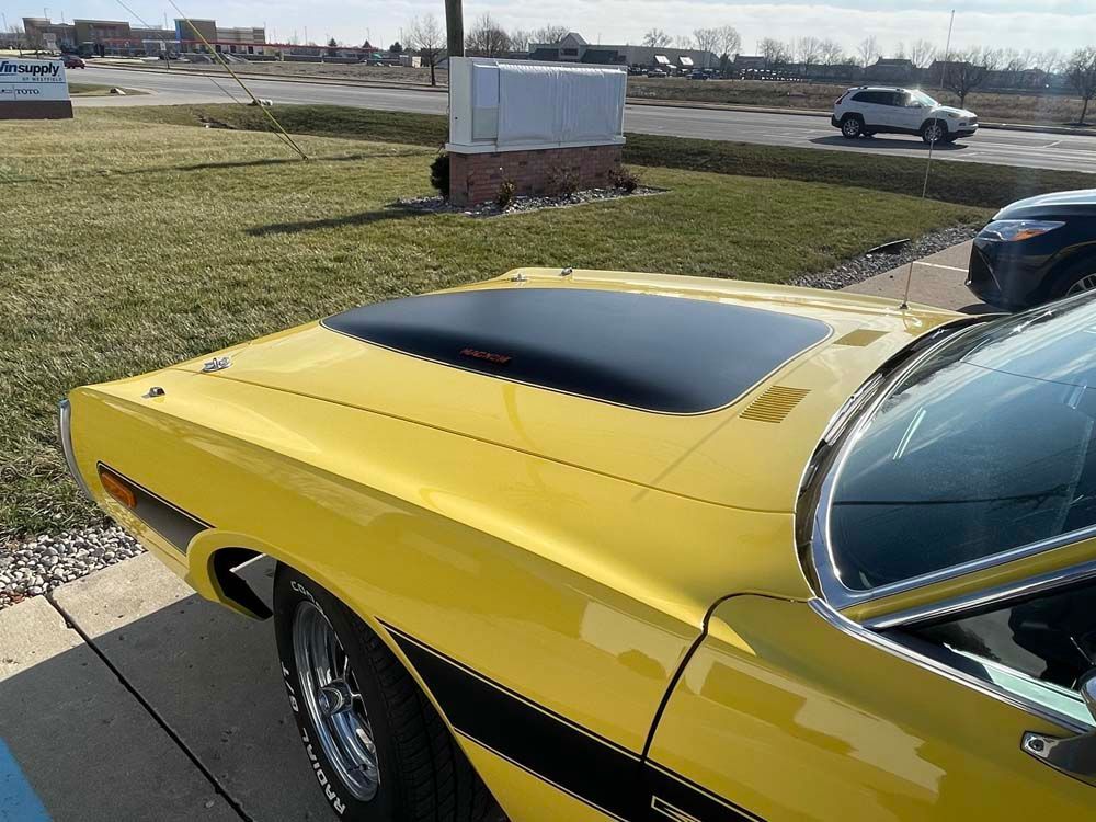 A yellow car with a black hood is parked in a parking lot.