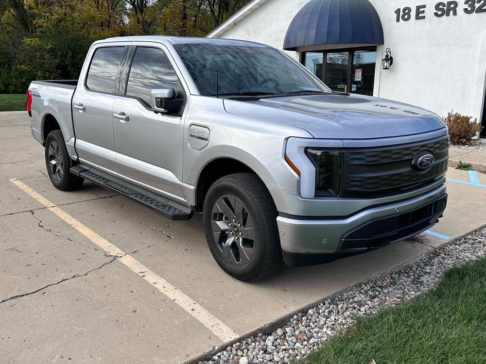 A silver ford f150 lightning pickup truck is parked in a parking lot in front of a building.