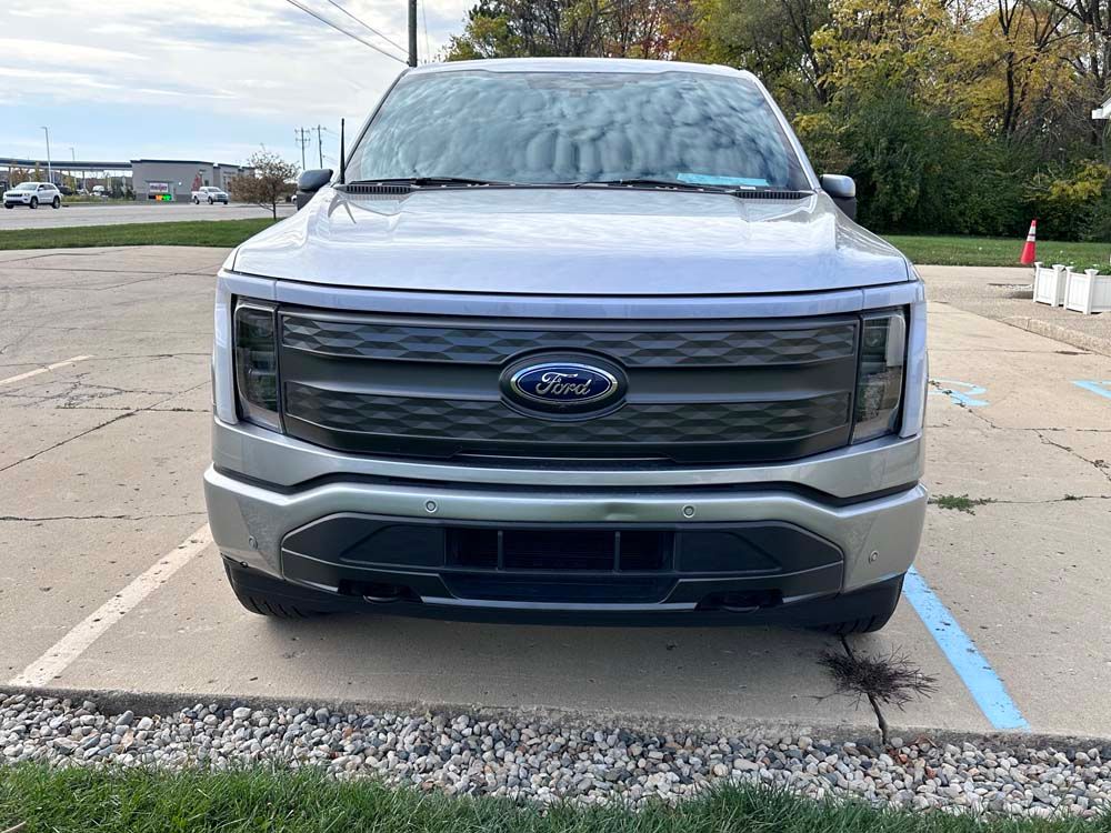 The front of a silver ford truck is parked in a parking lot.