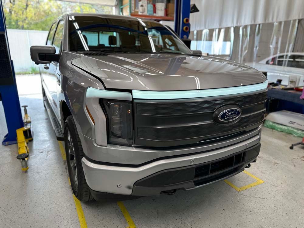 Silver Ford F-150 Lightning electric truck in a garage, showing the front with a blue light bar.