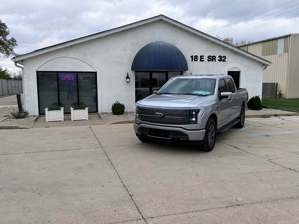 A silver pickup truck is parked in front of a white building.