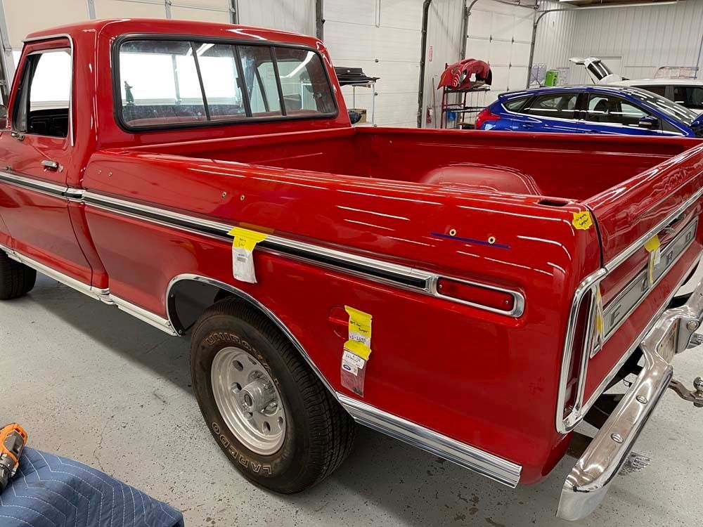 A red truck is parked in a garage next to a blue car.