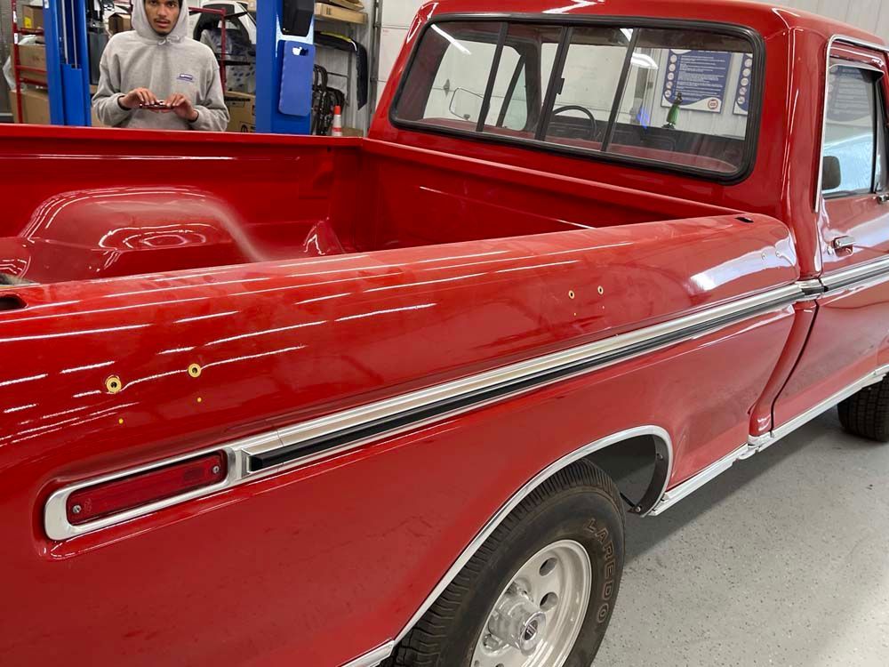 A man is standing next to a red truck in a garage.