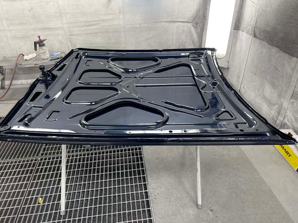 The hood of a car is being painted in a paint booth