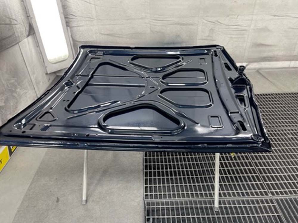 The hood of a car is being painted in a paint booth.