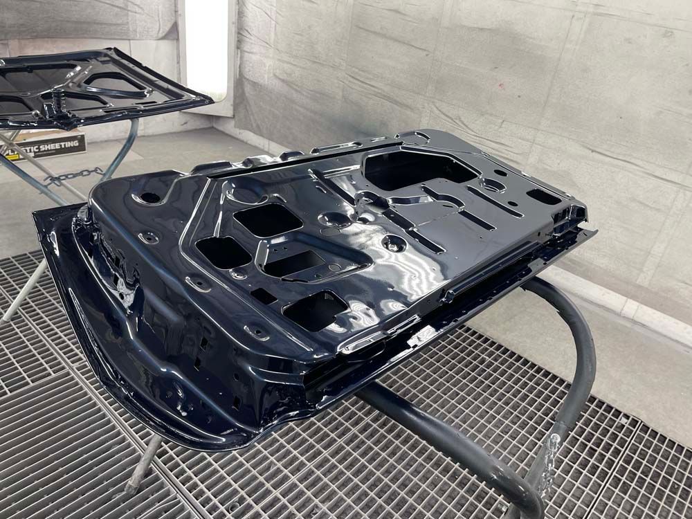 A black car door is sitting on a table in a paint booth.