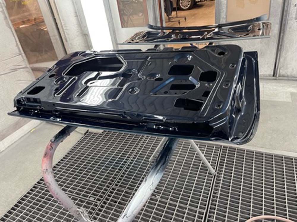 A black car door is being painted in a paint booth