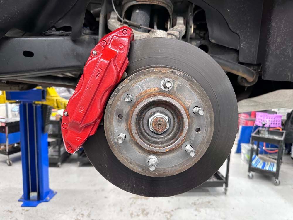 A car with a red brake caliper is sitting on a lift in a garage.