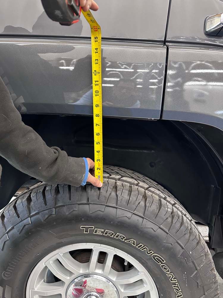 A person is measuring the height of a tire with a tape measure.
