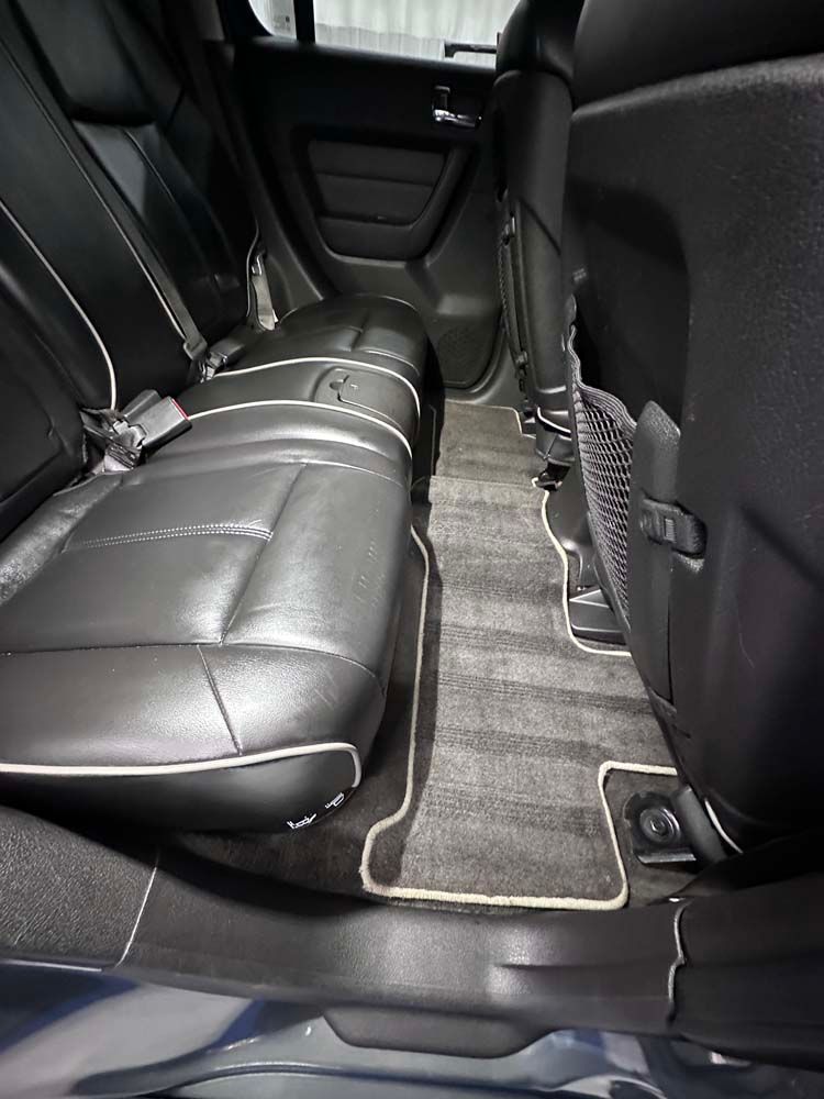 The back seat of a car with black leather seats and a carpeted floor.