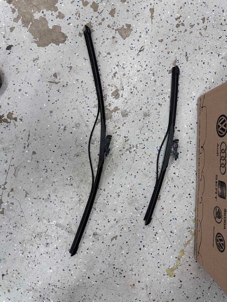 A pair of wiper blades are laying on the ground next to a box.