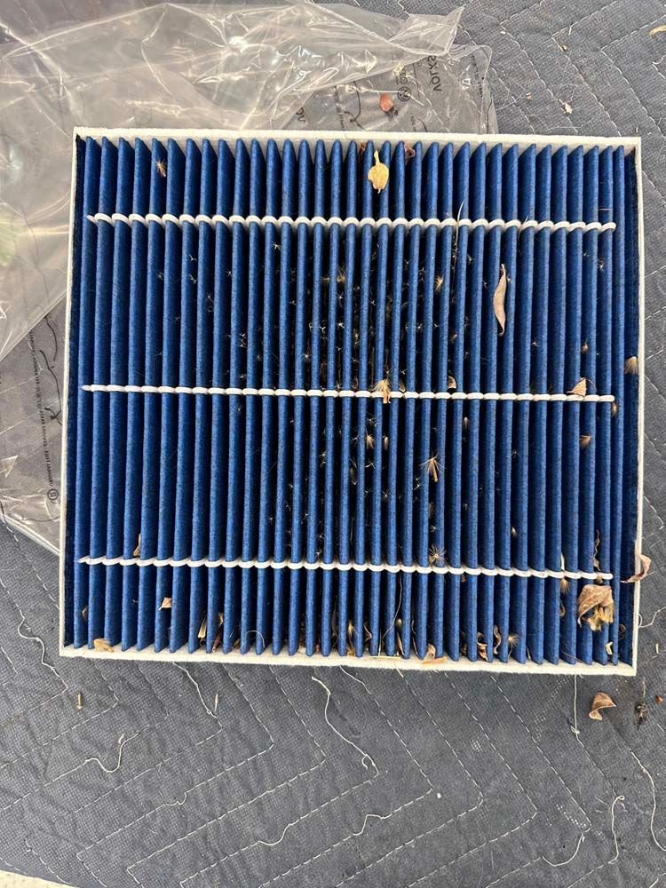 A dirty air filter is sitting on a quilted surface.