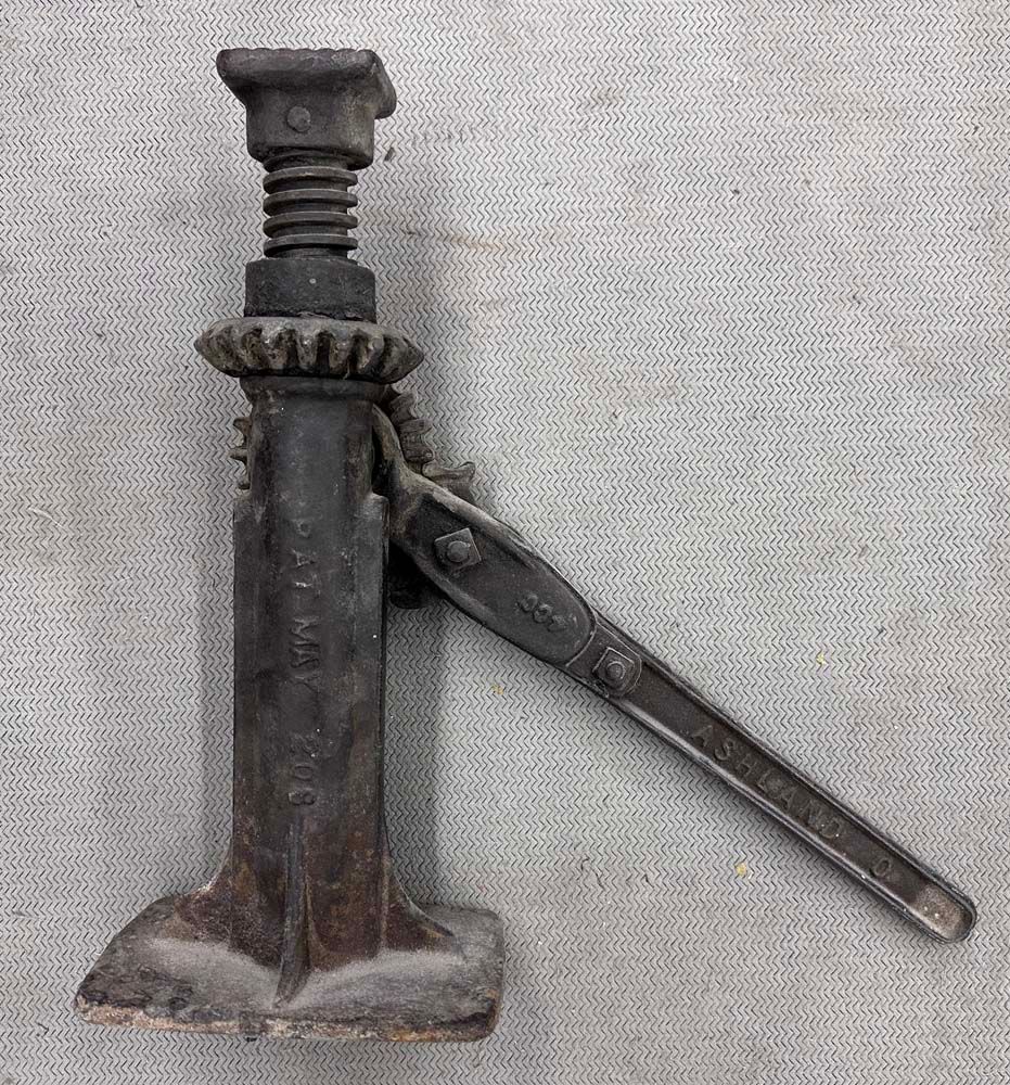 An old rusty jack is sitting on a concrete surface.