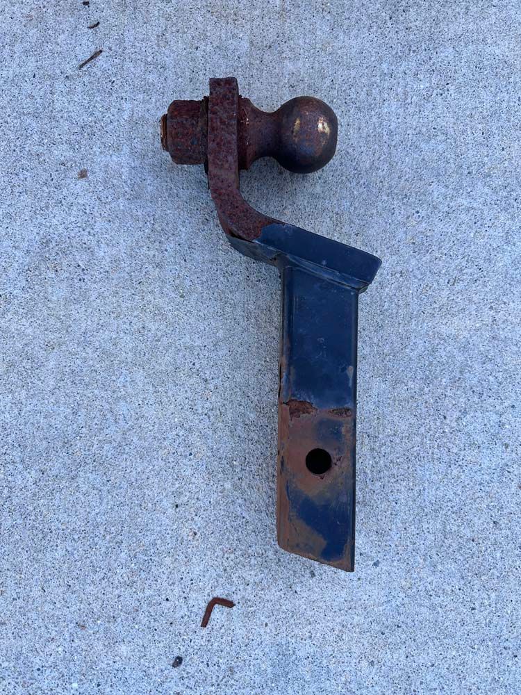 A rusty trailer hitch with a ball attached to it is sitting on a concrete surface.
