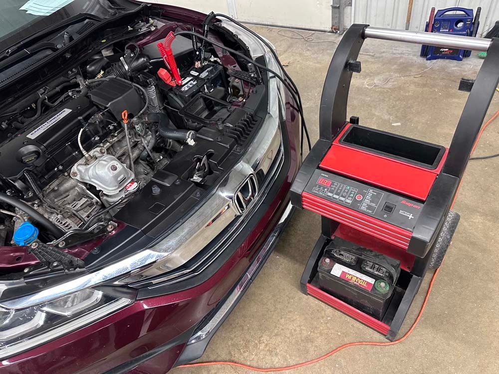 Red car engine bay with a battery charger cart.