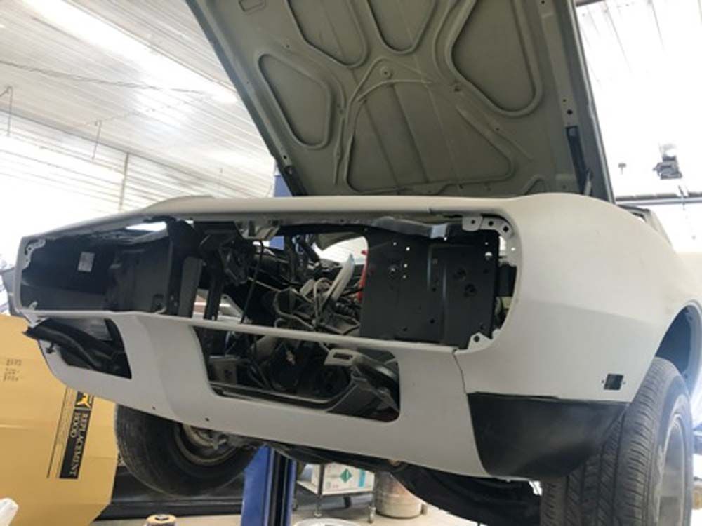 A car with the hood open is sitting on a lift in a garage.