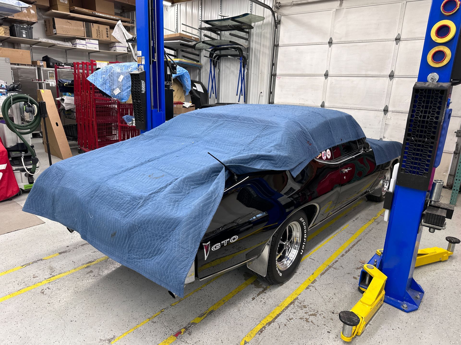 A black car with a blue cover on it is on a lift in a garage.
